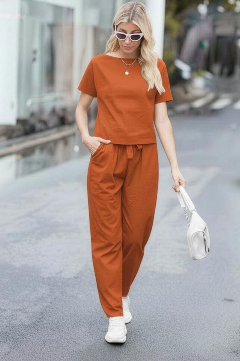 Woman wearing rust-colored cotton linen set with relaxed short-sleeve top and straight-leg pants walking outdoors