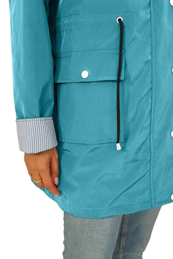 Close-up of blue water resistant windbreaker jacket pocket and sleeve with striped cuff detail on a person wearing jeans