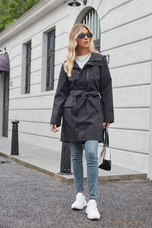 Woman wearing black water-resistant windbreaker trench coat with belt walking outdoors
