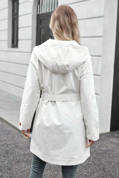 Back view of white water-resistant windbreaker trench jacket with hood and belt on woman outdoors
