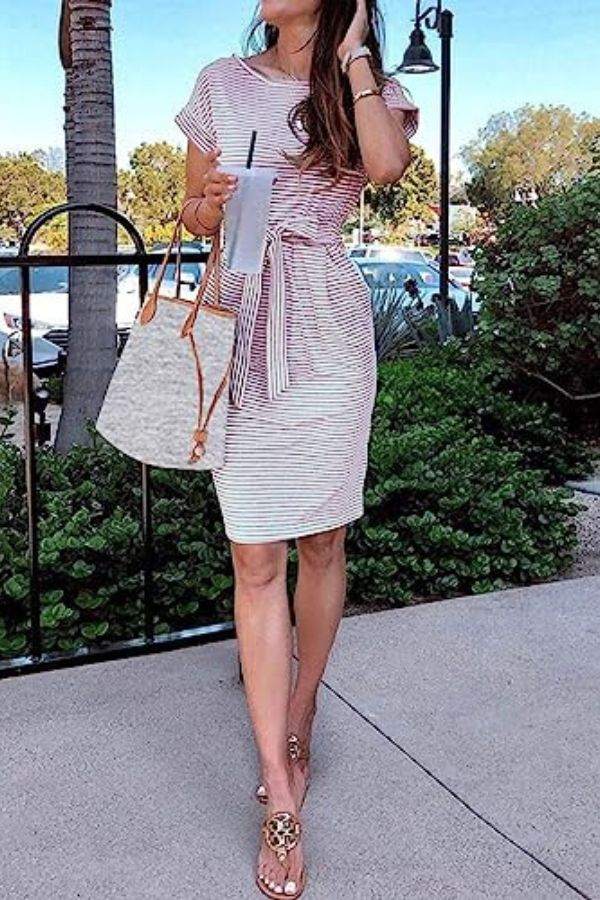 Woman wearing Airy Stripe Sheath Cotton Dress with tie belt and pockets, holding a drink and a tote bag outdoors