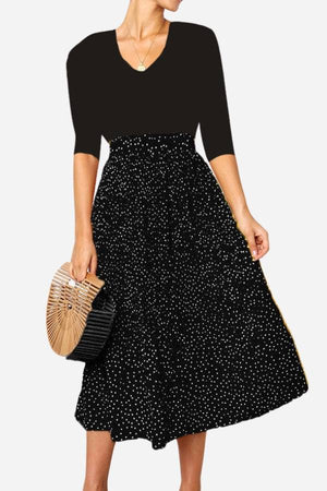 Woman wearing an effortlessly chic polka dot pleated high-waist midi skirt set with pockets and a black top holding a wooden handbag