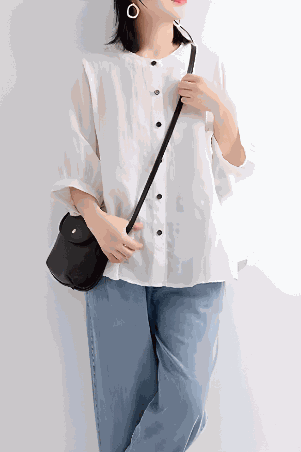 Woman wearing relaxed loose breathable white linen blouse with black buttons and blue jeans carrying a black purse