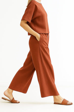 Rust-colored loose fit co-ord set with wide-leg pants and boxy short sleeve top, styled with flat sandals.