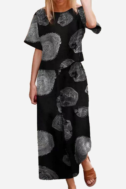 Woman wearing black loose fit co-ord set with grey circular tree ring patterns, featuring a boxy short sleeve top and wide-leg pants.