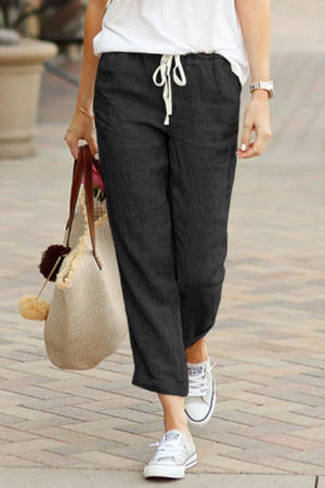 Woman wearing black relaxed fit straight pants with white drawstring and casual white sneakers walking outdoors carrying a beige tote bag