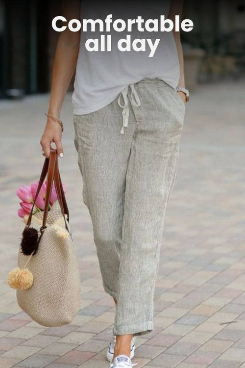 Woman wearing light gray relaxed fit straight pants walking outdoors with a beige handbag and white sneakers
