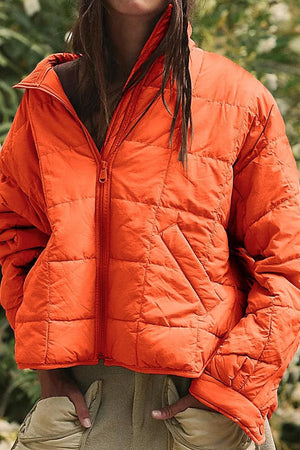 Orange lightweight puffer travel jacket with zip front and pockets, ideal for stylish and compact travel warmth.