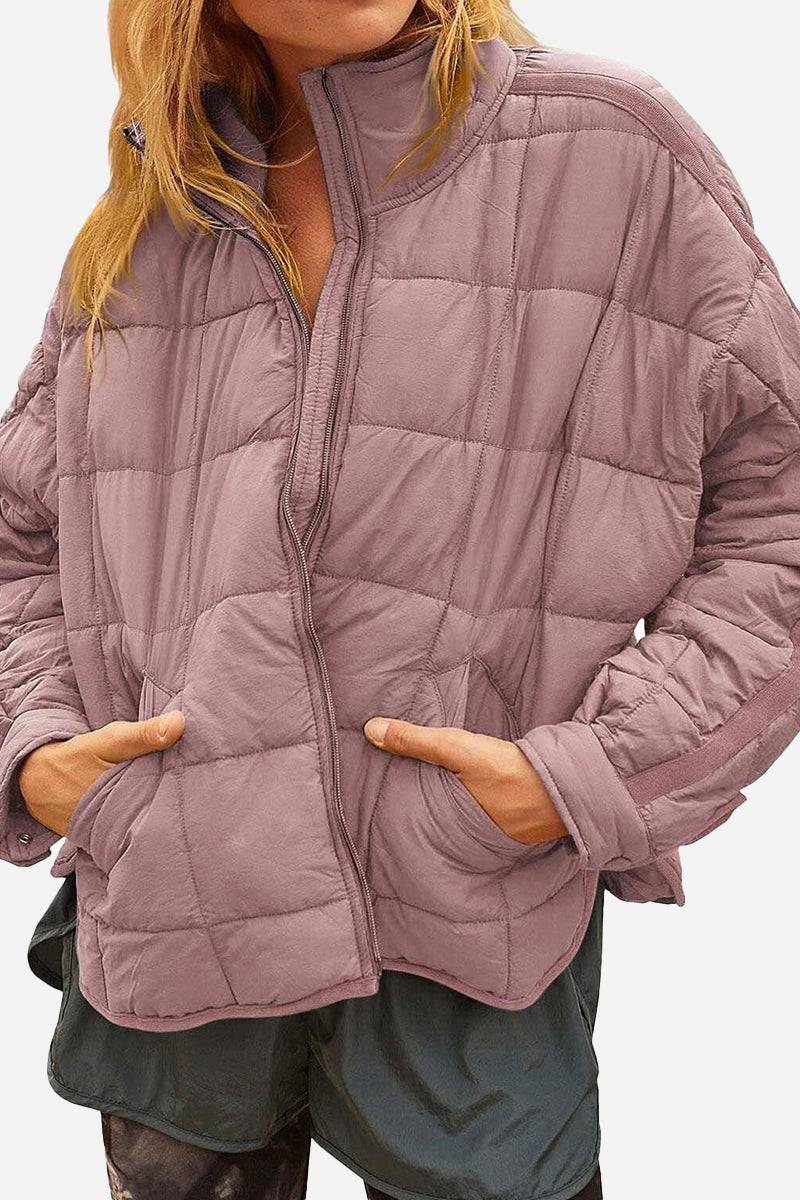 Woman wearing a mauve lightweight puffer travel jacket with front pockets and half-zip collar, styled for casual outdoor wear