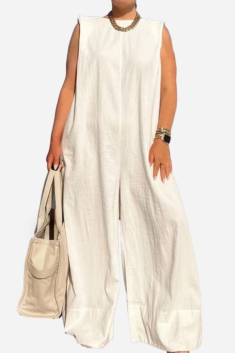 Woman wearing white sleeveless wide-leg jumpsuit with gold necklace and bracelets holding beige bag