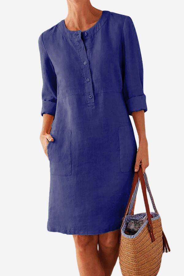 Blue cotton dress with 3/4 rolled sleeves, front buttons, and pockets, styled with a woven handbag.