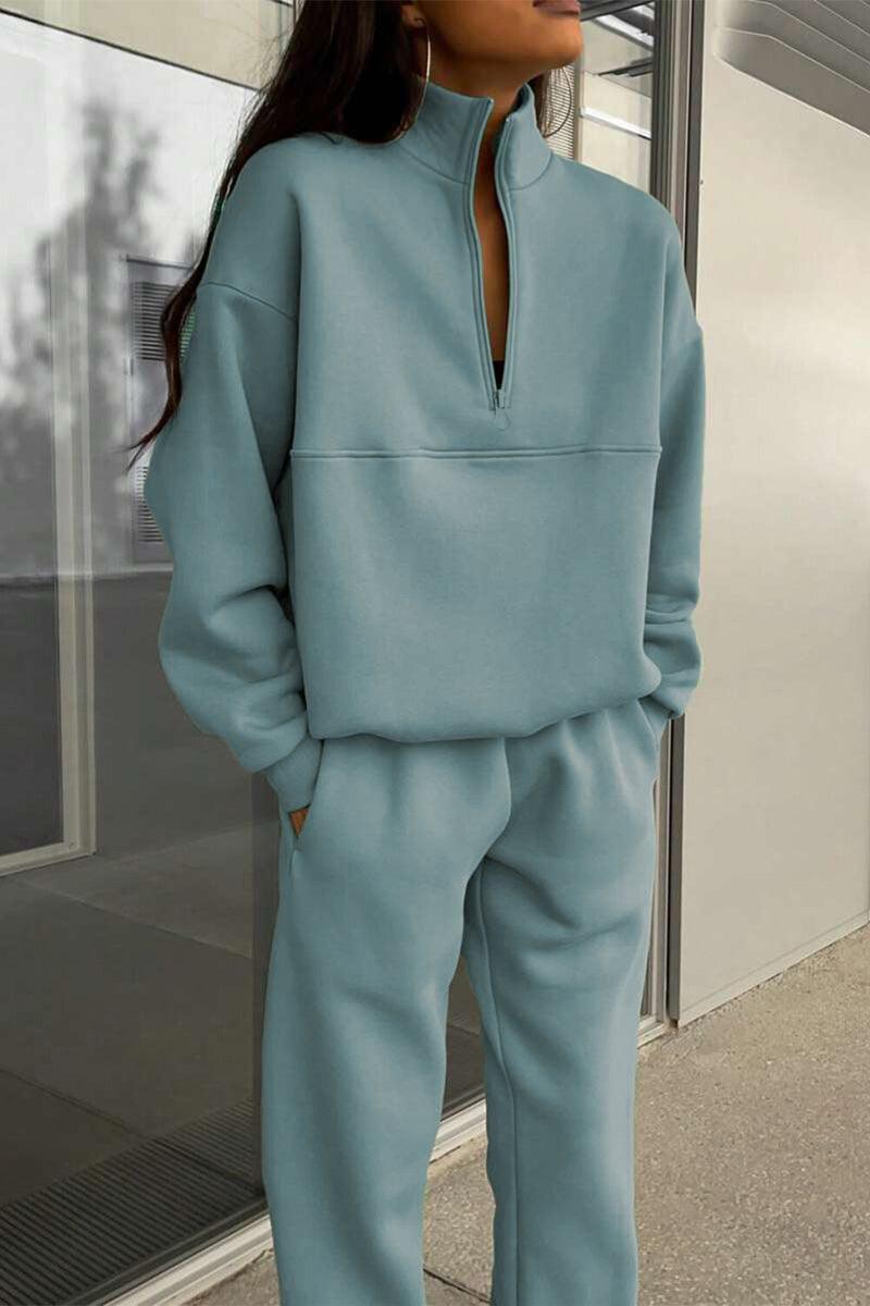 Woman wearing a light blue cotton-blended two-piece tracksuit with high collar and deep zipper standing outdoors.