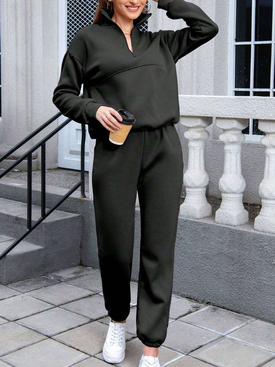 Woman wearing black cotton-blended two-piece tracksuit with high collar and zipper, holding coffee cup outdoors