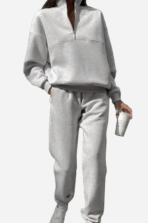 Woman wearing grey cotton-blended two-piece tracksuit with high collar and zipper, holding a cup