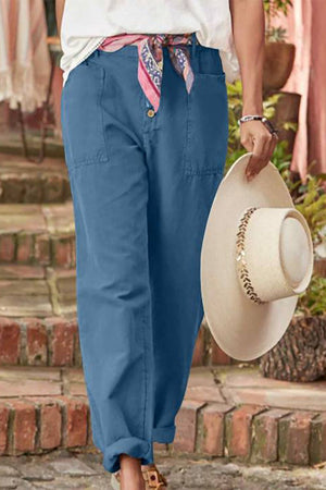Blue casual button-down utility-chic trousers with pockets and rolled cuffs worn with a white top and holding a beige hat