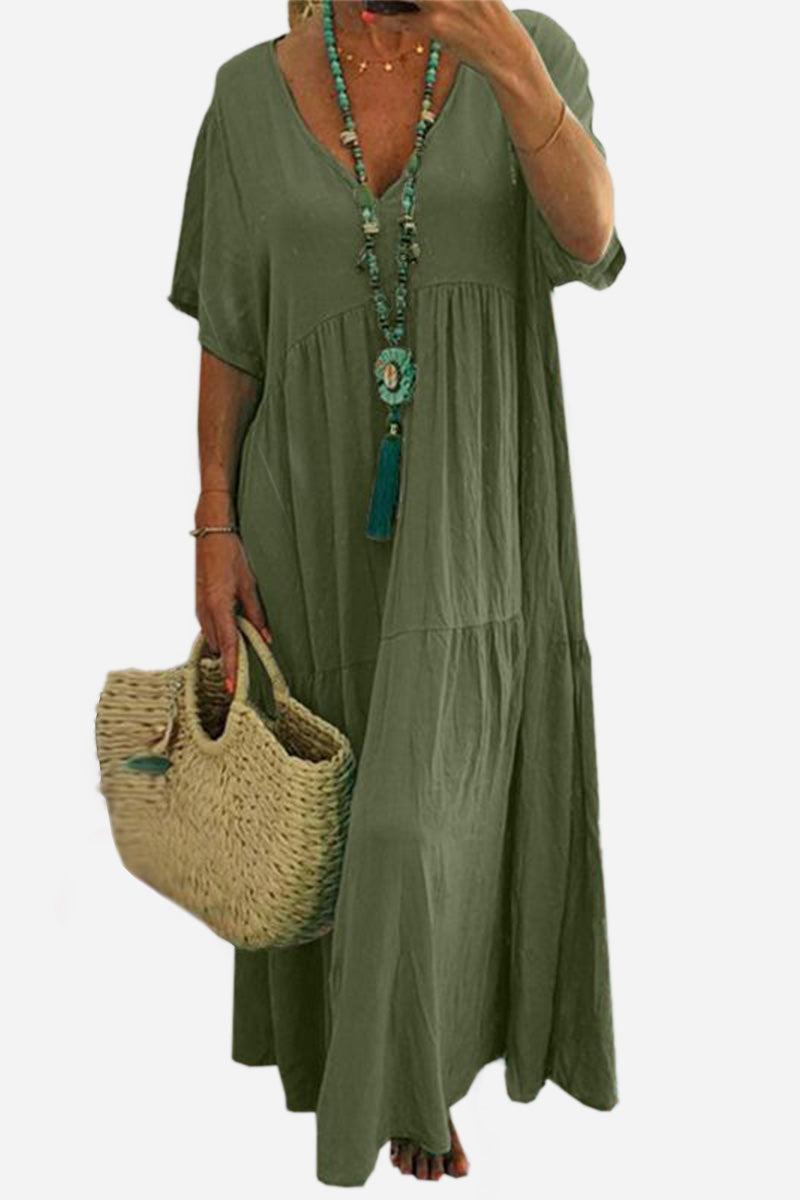 Olive green V-neck two-tiered maxi swing dress with loose sleeves and flowing silhouette, worn with beaded necklace and straw handbag.