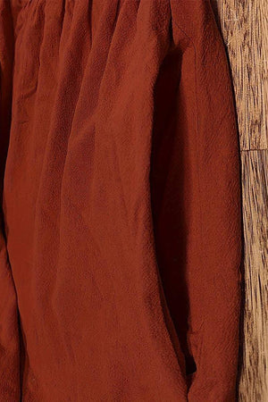 Close-up of rust-colored capped-sleeve voluminous pleated midi dress fabric and pocket detail on wooden floor