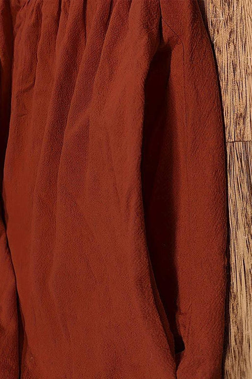 Close-up of rust-colored capped-sleeve voluminous pleated midi dress fabric and pocket detail on wooden floor