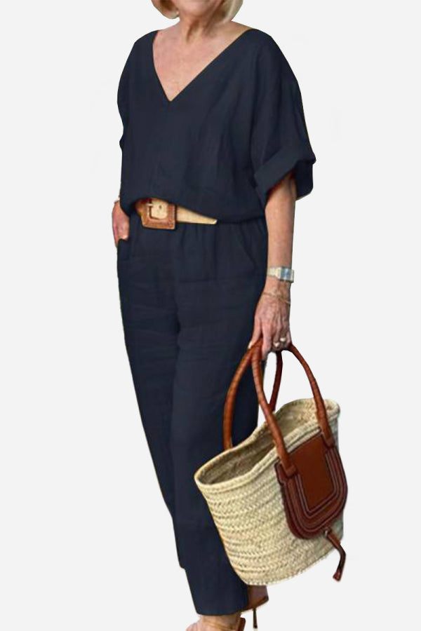 Woman wearing navy V-neck cotton two-piece trouser set holding woven handbag