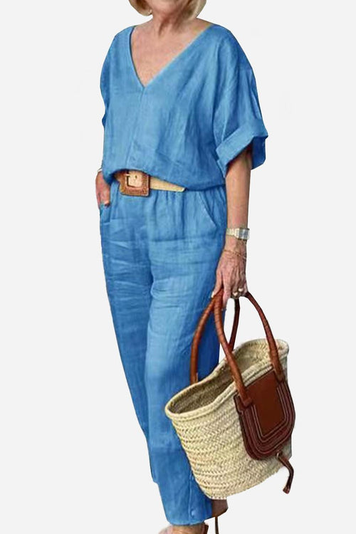 Woman wearing blue V-neck cotton two-piece trouser set with rolled sleeves and carrying a woven straw handbag.