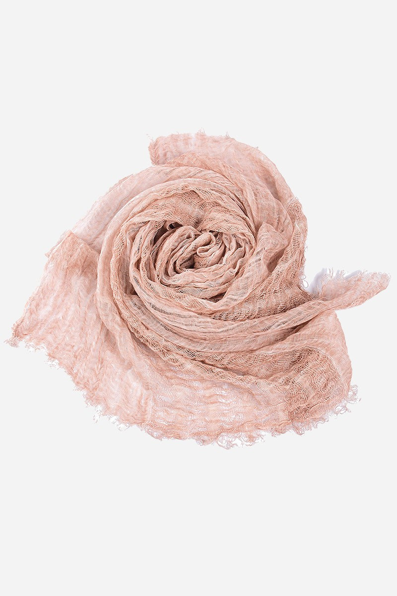 Soft pink lightweight linen scarf with frayed edges rolled in a spiral shape on a white background