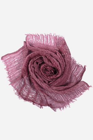 Lightweight linen scarf in soft mauve with frayed edges, rolled in a rose shape on white background