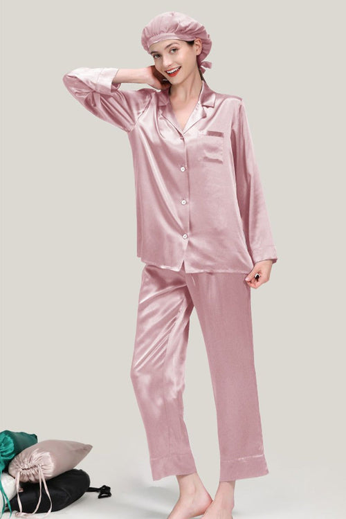 Woman wearing classic pink Mulberry silk pajama set with matching sleep cap, standing on neutral background