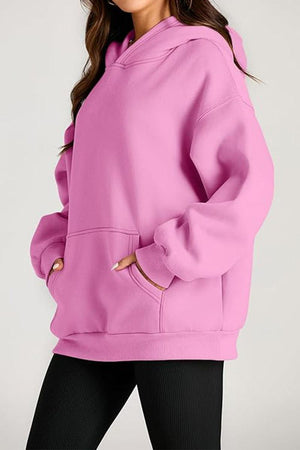 Woman wearing a pink oversized fleece-lined hoodie with front pocket and relaxed fit