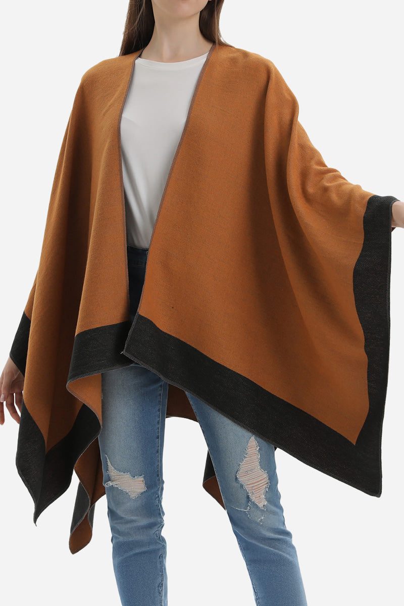 Elegant knitted poncho in two-tone brown and black, lightweight and flowy, styled casually with jeans.