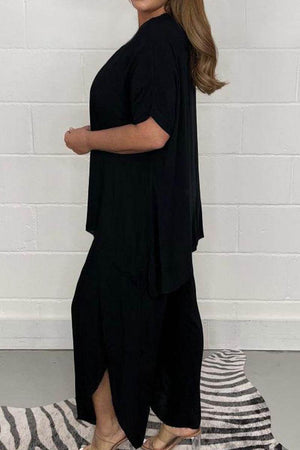 Woman wearing black relaxed linen-like travel 2-piece set with loose fit and split hem pants against a white wall