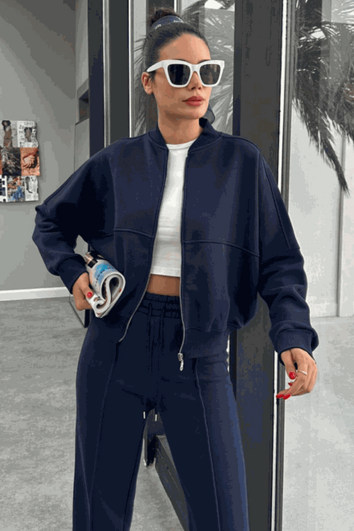 Woman wearing The Voyager Zip Set navy blue zip-front sweatshirt and wide-leg joggers, styled with white crop top and sunglasses