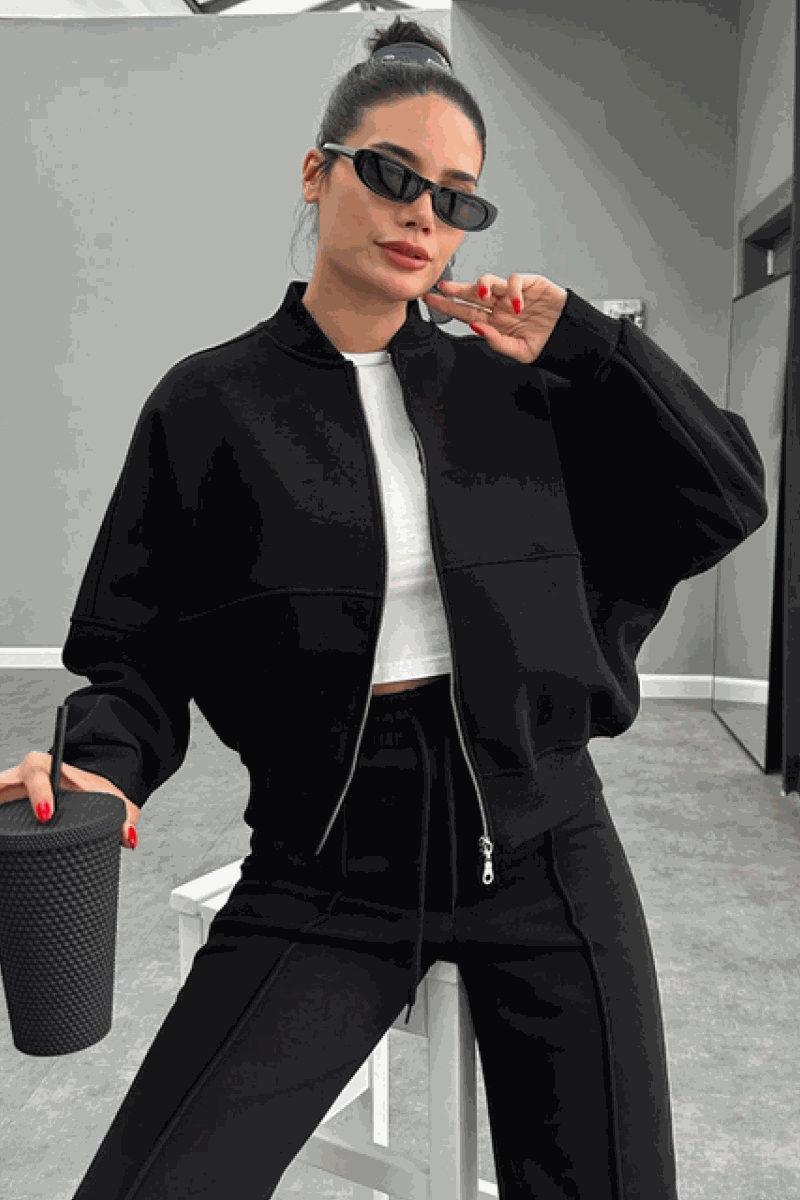 Woman wearing The Voyager Zip Set black zip-front sweatshirt and wide-leg joggers holding a cup, styled for travel and casual comfort.