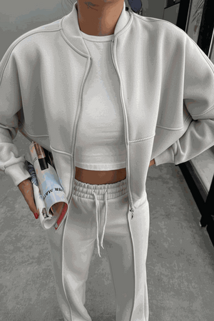 Woman wearing The Voyager Zip Set white zip-front sweatshirt and wide-leg joggers holding a magazine in a modern indoor setting