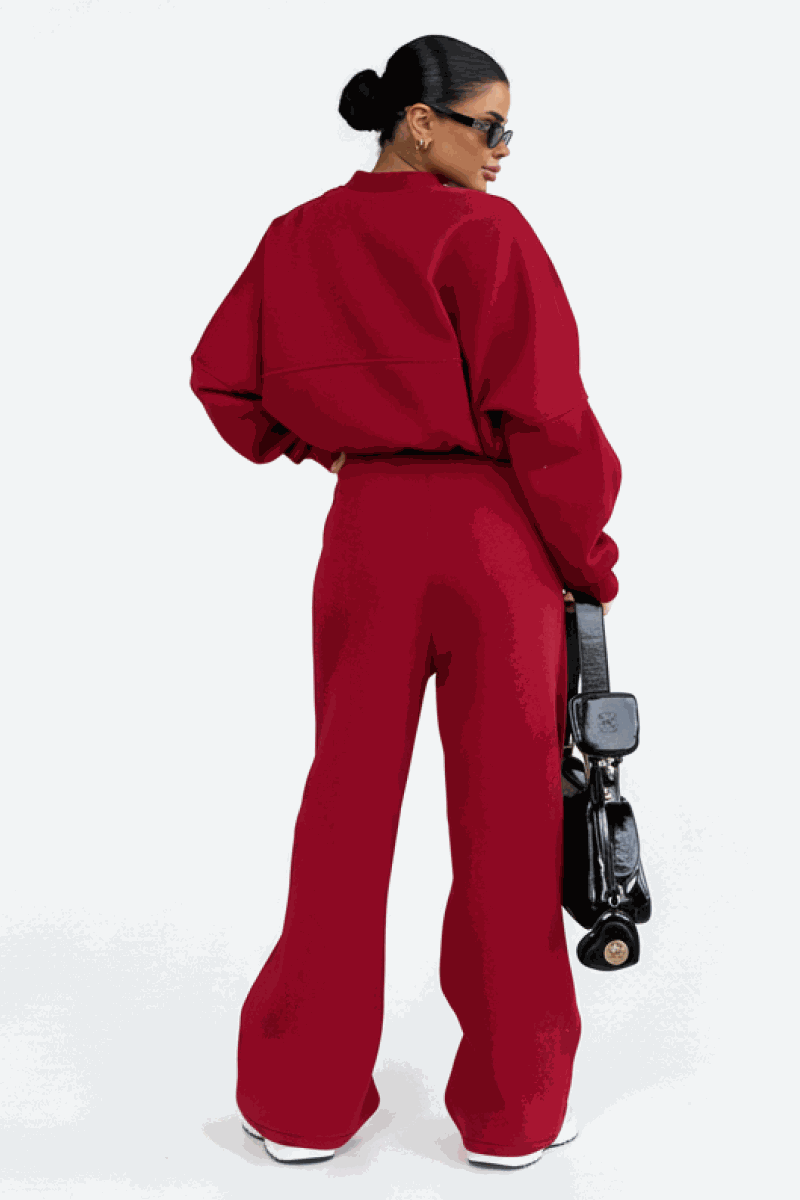 Woman wearing The Voyager Zip Set in red, featuring a relaxed zip-front sweatshirt and wide-leg joggers with pockets, styled with black bag and sneakers.