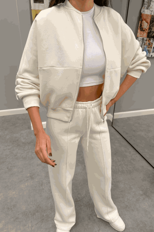 Woman wearing The Voyager Zip Set cream zip-front sweatshirt and wide-leg joggers with pockets, styled with a white crop top and sneakers.
