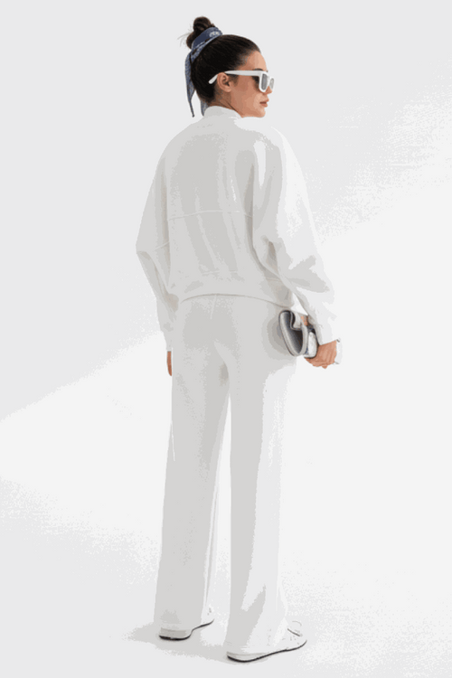 Woman wearing white Voyager Zip Set with zip-front sweatshirt and wide-leg joggers, styled with sunglasses and hair scarf, standing against white background
