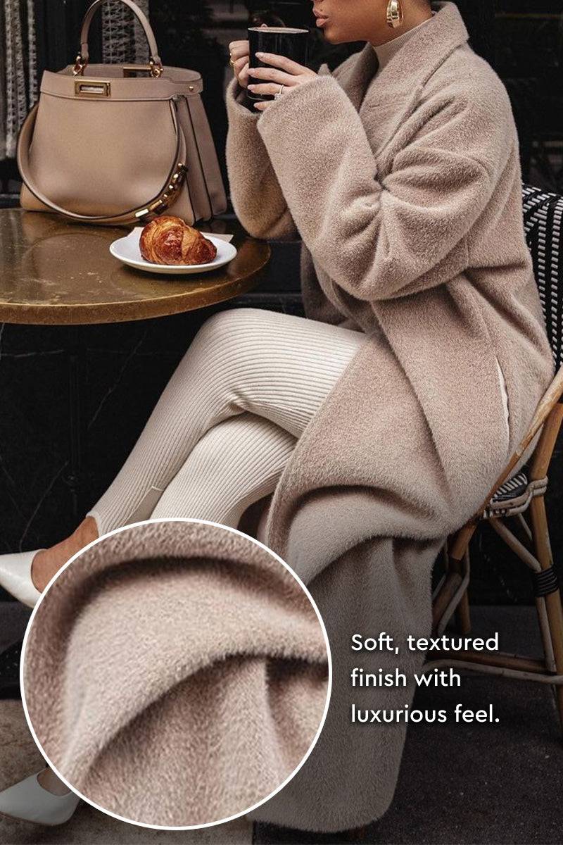 Woman wearing oversized teddy coat sitting at cafe table with croissant and handbag, close-up of soft textured fabric