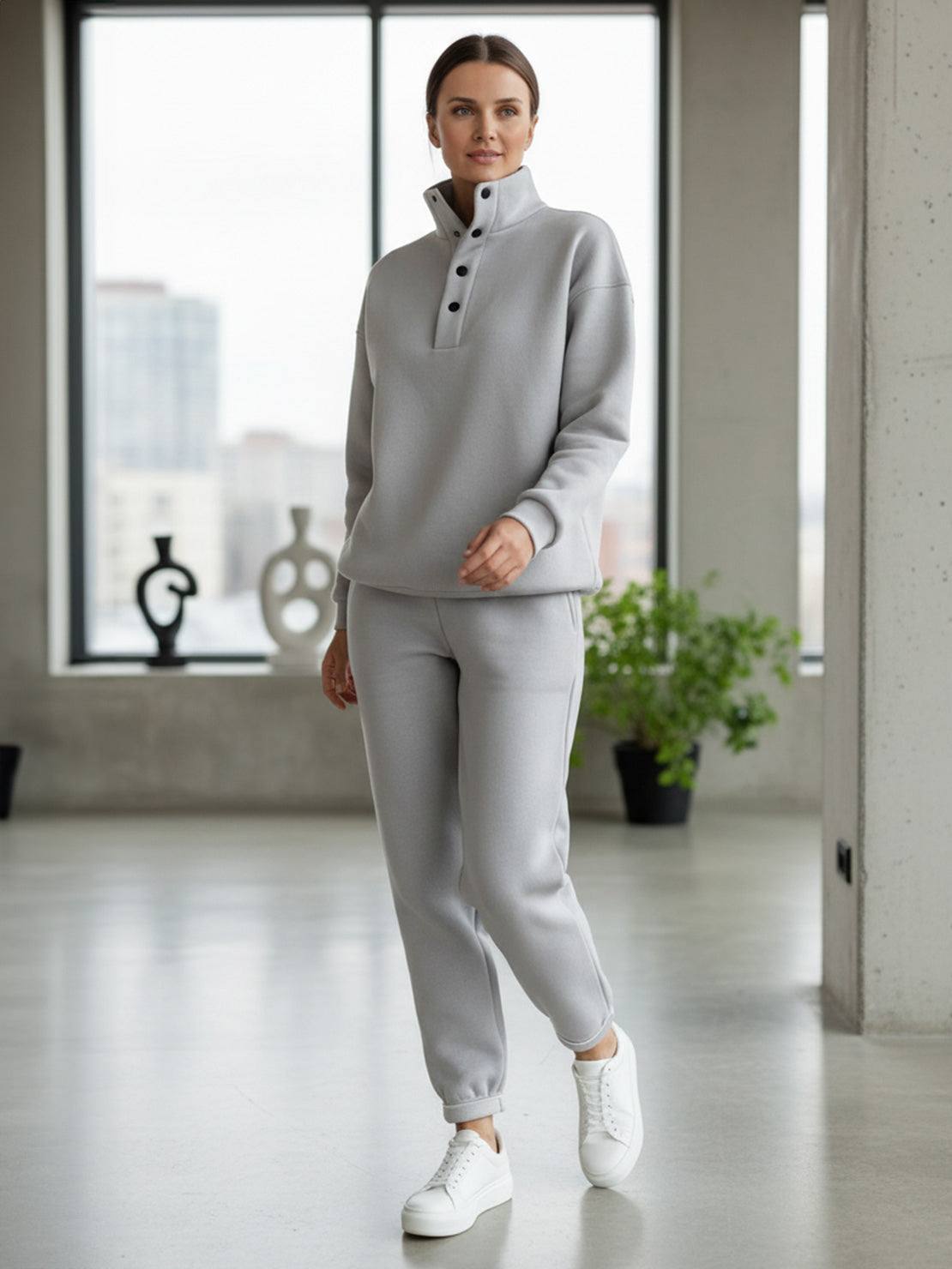 Woman wearing a grey warm and easy two-piece set with pullover hoodie and matching pants in a bright indoor setting