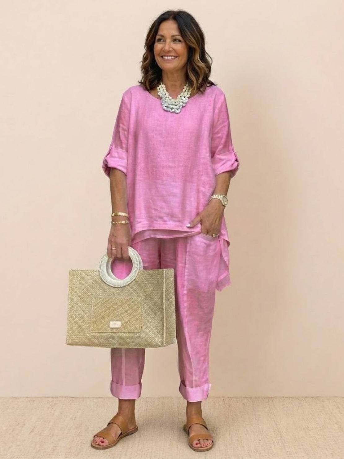 Woman wearing pink asymmetrical two-piece trouser set with rolled-up sleeves and tapered pants holding a woven handbag