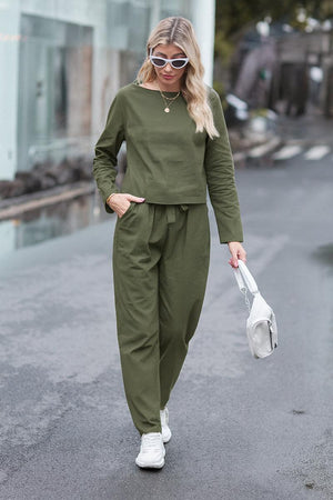 Woman wearing olive green cotton-linen monochrome longline top and wide-leg pants set walking outdoors with white sneakers and sunglasses