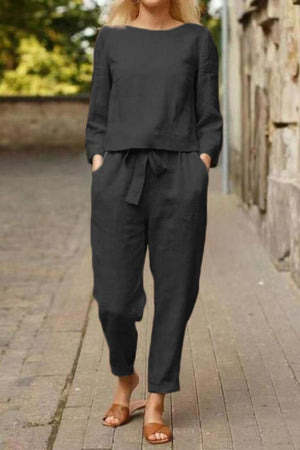 Woman wearing a black Cotton-Linen Monochrome Capsule relaxed longline top and wide-leg pants set with a tie waist, standing outdoors on a paved street.