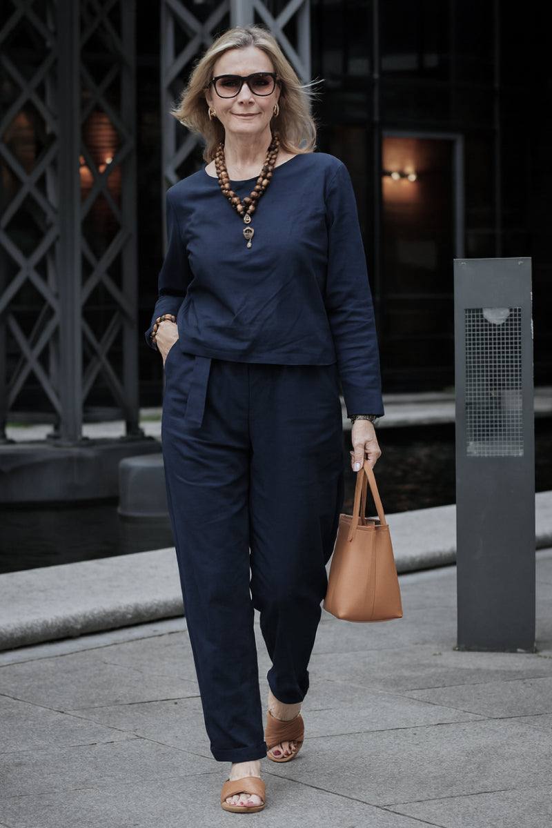 Woman wearing navy cotton-linen monochrome capsule outfit with longline top and wide-leg pants, accessorized with brown handbag and sandals.