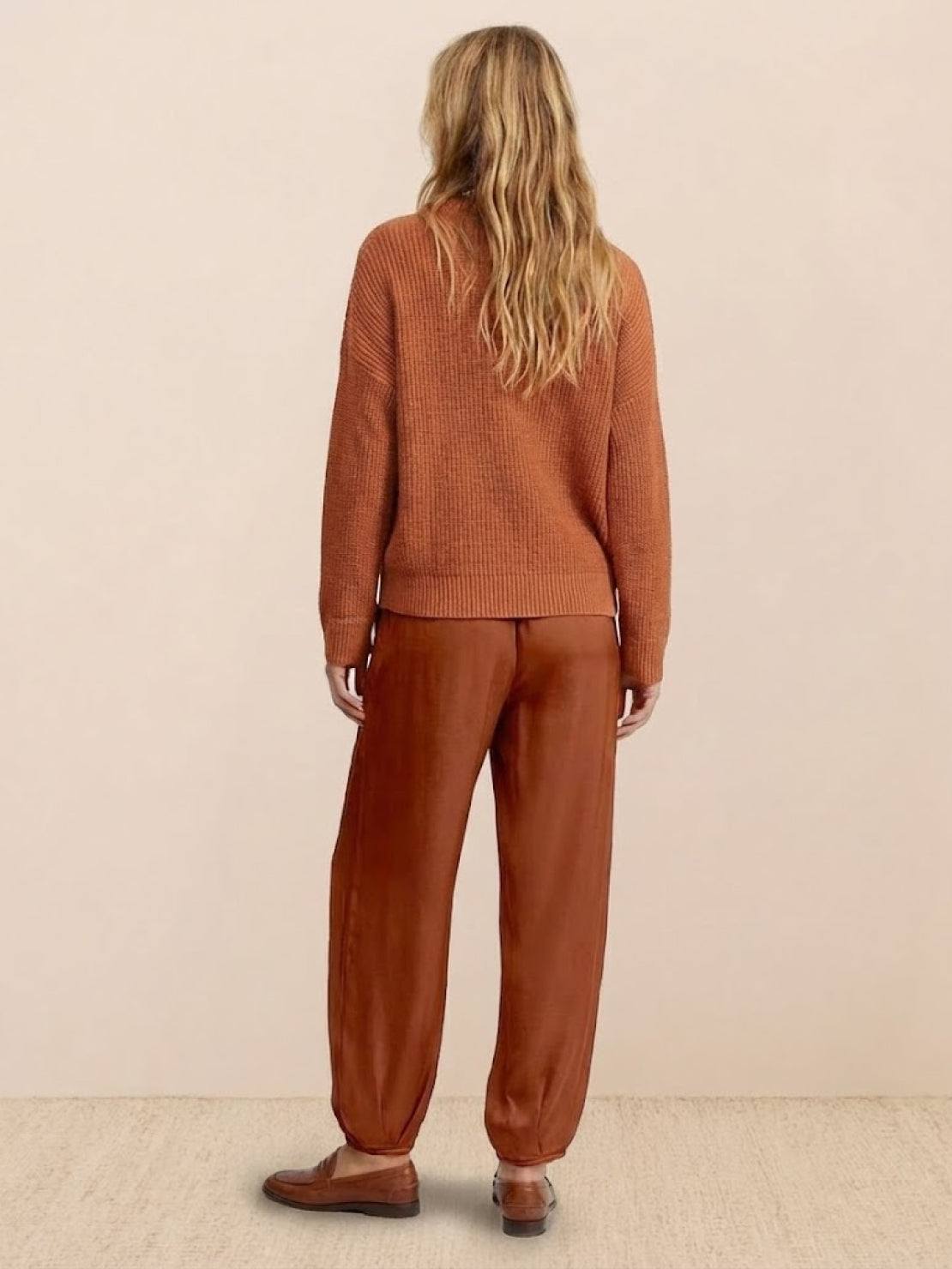 Woman wearing European Minimalism relaxed knit sweater and drapey trousers set in earthy brown tones back view