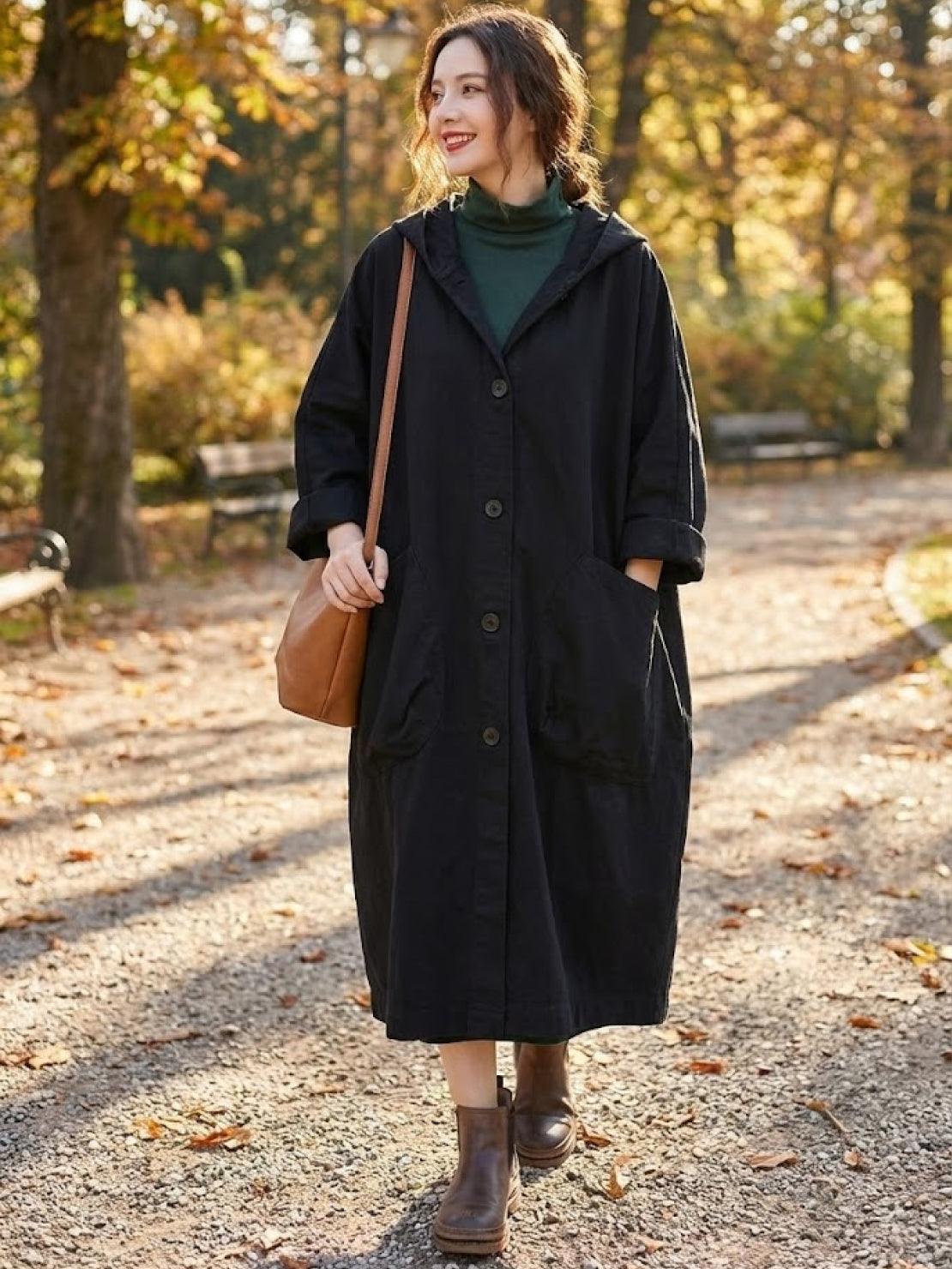 Woman wearing oversized black water-resistant windbreaker jacket with hood, large pockets, and snap-button closure in autumn park setting