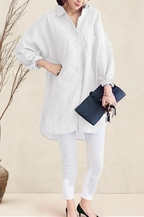 Woman wearing oversized linen shirt in white with rolled-up sleeves, paired with white pants and black heels, holding a black clutch.
