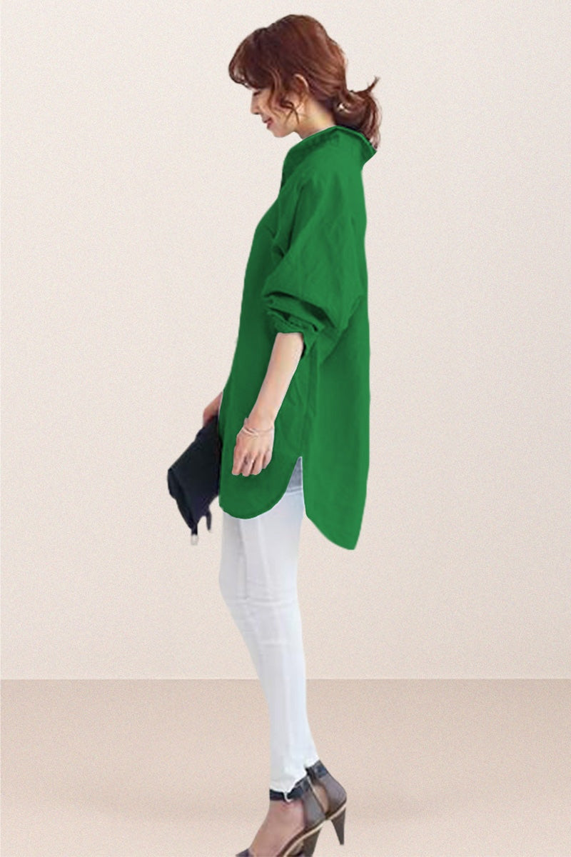 woman wearing green oversized linen shirt with rolled sleeves and white pants standing sideways holding black clutch