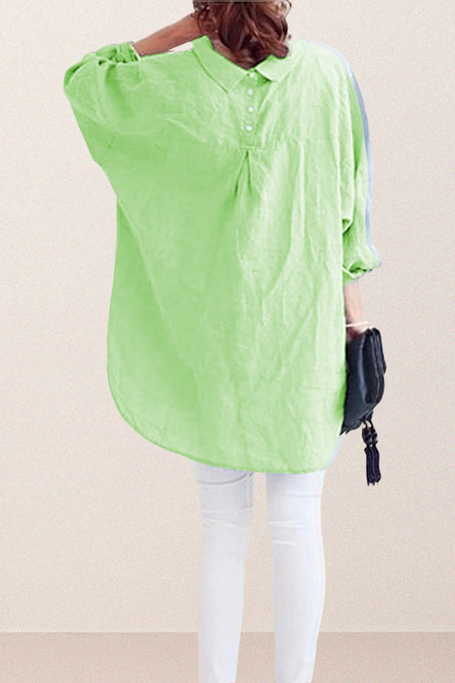 Back view of a woman wearing a light green oversized linen shirt with button and gathered detailing, paired with white pants and holding a black clutch bag