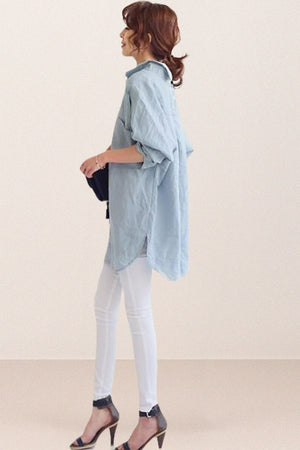 Side view of woman wearing oversized linen shirt in light blue with rolled sleeves and white pants
