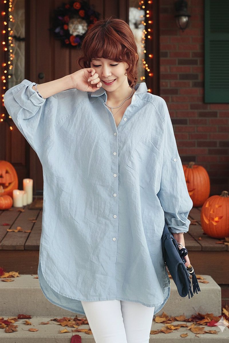 Woman wearing light blue oversized linen shirt with Halloween pumpkins and lights in background