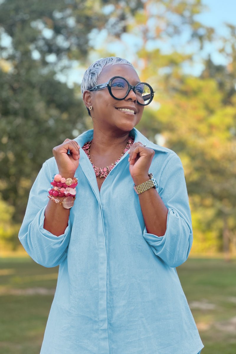 Woman wearing oversized 100 cotton light blue shirt outdoors with sunglasses and jewelry